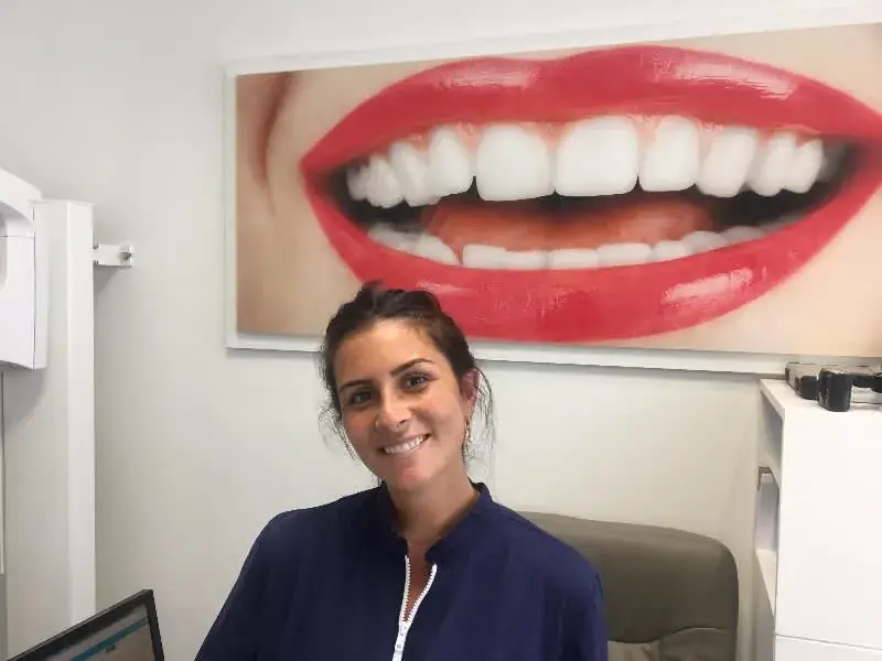 Le Dr Laura Zeitoun Saal devant une grande photographie encadrée d’un sourire, dans une salle de soins du cabinet